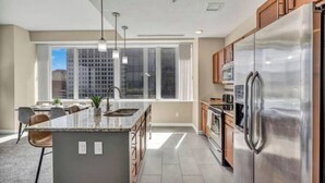 Una cocina moderna con una isla grande, electrodomésticos de acero inoxidable y vistas a la ciudad a través de amplios ventanales.