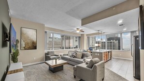 A spacious living room with a large sofa, a coffee table, and a TV mounted on the wall.