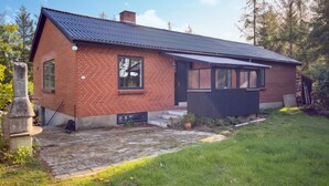 Une maison de plain-pied en briques, avec un toit en métal à pente, un petit porche doté d’une porte sombre et une cheminée en briques.
