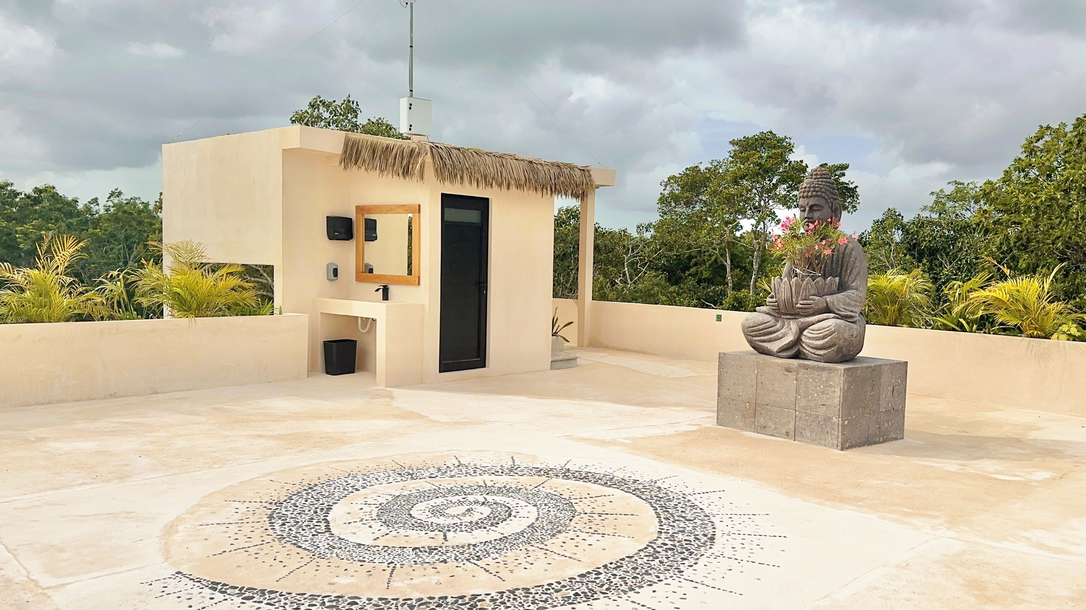 A modern building with a thatched roof structure, a central door, and a circular mosaic on the ground.