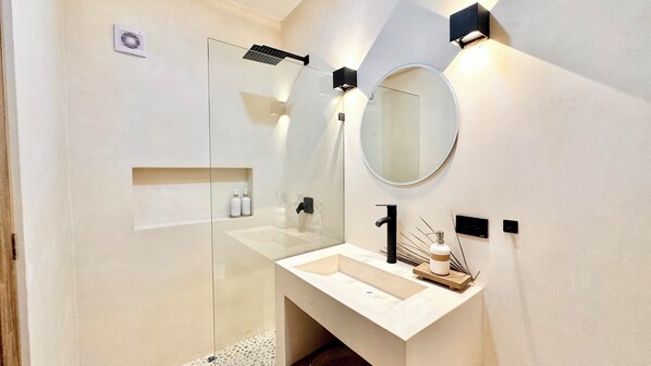 A modern bathroom with a glass shower enclosure, a round mirror, and a minimalist sink area. - COCAY PI By SANDY POWERFUL (Tulum)