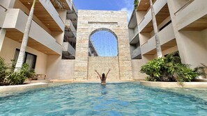 A pool area with a central archway, surrounded by buildings with balconies and potted plants. - COCAY PI By SANDY POWERFUL (Tulum)
