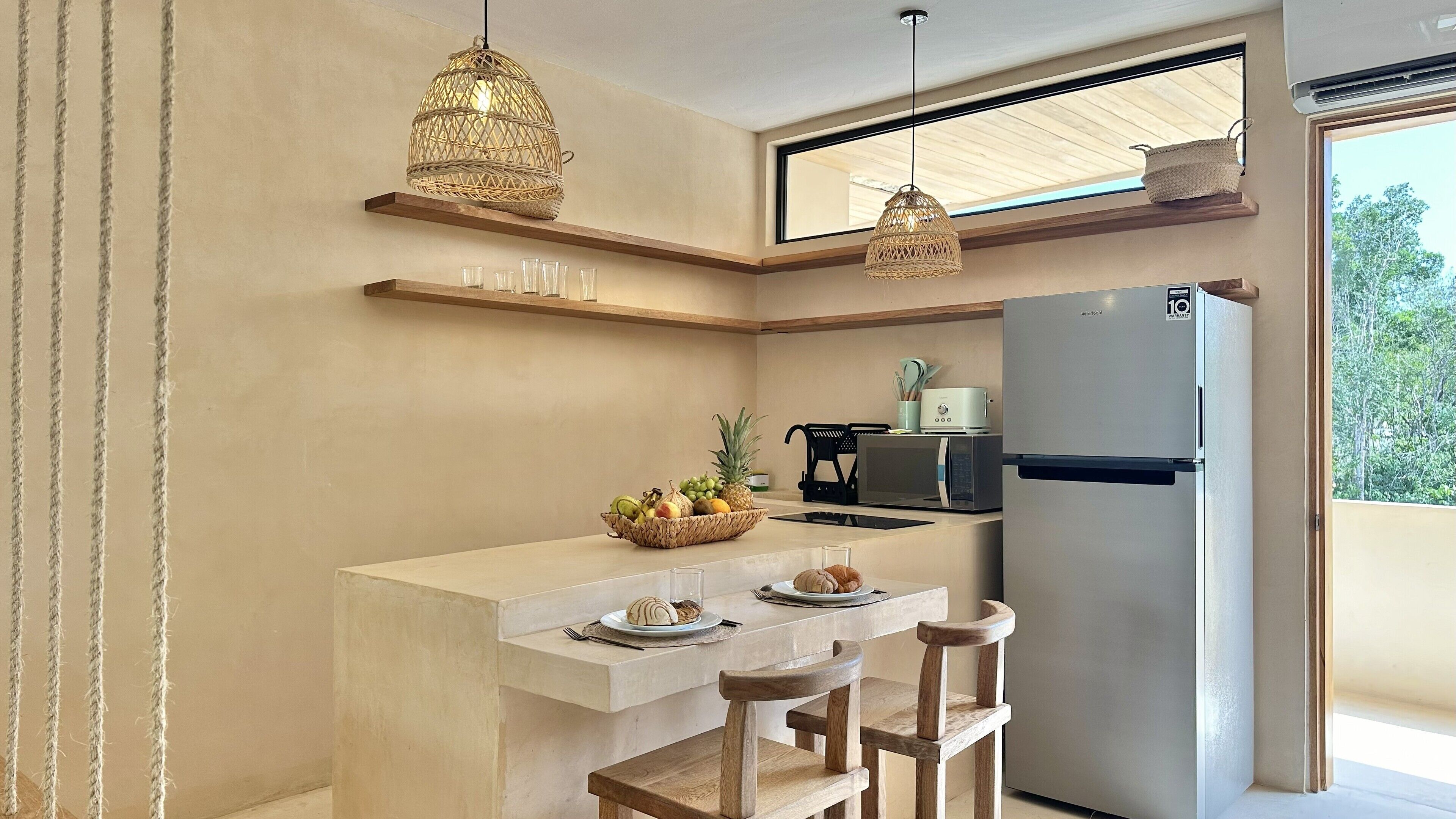 A modern kitchen with a built-in refrigerator, a dining area with a wooden bench, and a hanging light fixture.