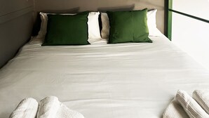 A neatly made bed with white bedding and two green pillows, and two rolled white towels on the side.