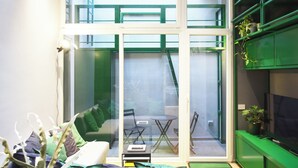 A room with a glass door leading to an outdoor area, a small table with chairs, and a TV on a green stand.