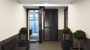 A hallway with a bench, two potted trees, a door, and a view into another room.