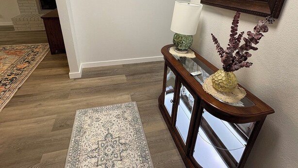 A hallway with a patterned rug, a wooden console table with a vase, a mirror, and decorative wall art. - Jennie May's Retreat offers a comfortable place to rest and recharge! (Enid)