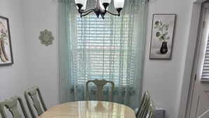 A dining area with a round wooden table, green chairs, a floral-patterned rug, and a chandelier. - Jennie May's Retreat offers a comfortable place to rest and recharge! (Enid)