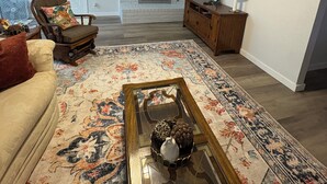 A living room with a ceiling fan, a flat-screen TV, a fireplace, a sofa, a coffee table, and a patterned rug. - Jennie May's Retreat offers a comfortable place to rest and recharge! (Enid)