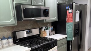 A kitchen with a stove, oven, microwave, refrigerator, and green cabinets. There are utensils and a coffee maker on the counter. - Jennie May's Retreat offers a comfortable place to rest and recharge! (Enid)