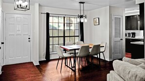 Un comedor con una mesa y sillas de madera, una araña y vistas a través de un gran ventanal.