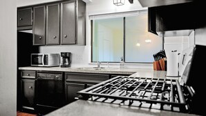 Una cocina moderna con armarios oscuros, microondas, cafetera y estufa a gas.