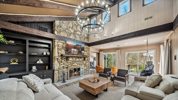 A spacious living room with a stone fireplace, modern furniture, and a large window overlooking a deck.