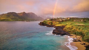 A coastal resort with a view of the ocean, a rainbow, and a mountainous backdrop.