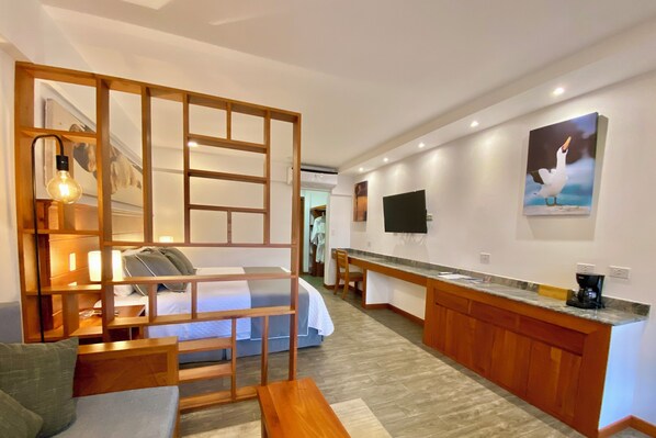 Habitación de hotel con cama, separador de madera, escritorio y un cuadro de un pájaro.