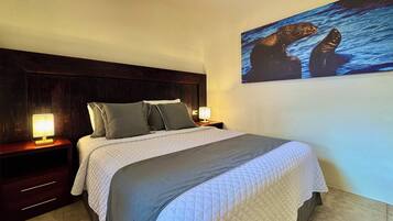 A bedroom with a large bed, two bedside tables with lamps, a dark wood headboard, and a wall-mounted painting of two seals.
