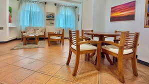 A dining area with wooden chairs and a table, a sofa, and curtains. - Spacious two-bedroom suite with a balcony (Puerto Ayora, Santa Cruz Island)