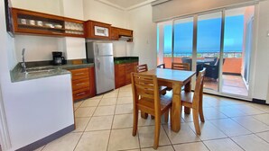 A kitchen with wooden cabinets, a refrigerator, and a dining table with chairs. - Ocean view Penthouse (Puerto Ayora, Santa Cruz Island)