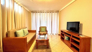 A living room with a sofa, armchair, coffee table, TV stand, and curtains. - One Bedroom with private balcony (Puerto Ayora, Santa Cruz Island)