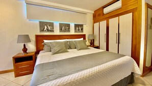 A neatly made bed with a grey and white duvet, wooden headboard, and bedside tables with lamps. There are three framed pictures on the wall above the bed. - One Bedroom with private balcony (Puerto Ayora, Santa Cruz Island)