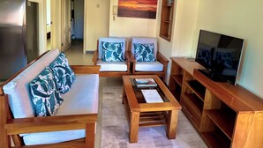 Un salon comprenant un canapé, deux fauteuils, une table basse, un téléviseur et une bibliothèque.