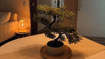 A room with a bonsai tree on a table, a lamp, and a door in the background.