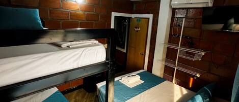 A dormitory room with bunk beds, a brick wall, a wooden floor, and a ceiling fan.