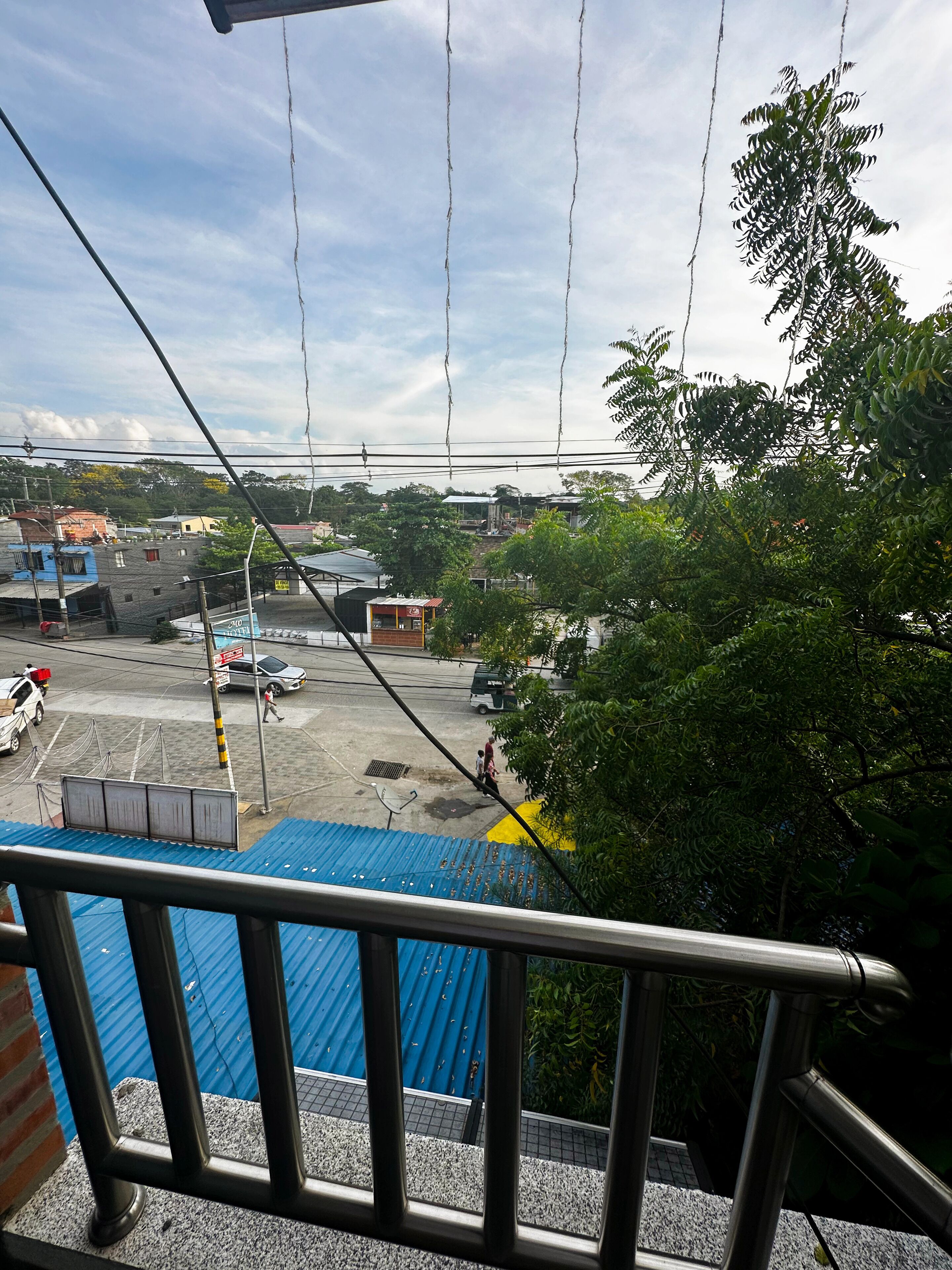 Vista de uma varanda com vista para um estacionamento, um edifício com telhado azul, uma tenda amarela e um pequeno quiosque.