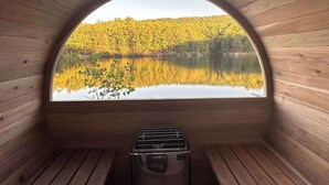 Une cabane en bois dotée d’une grande fenêtre en arc qui donne sur un lac et une forêt.