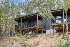 Una cabaña moderna con terraza de madera y ventanas grandes, rodeada de árboles.