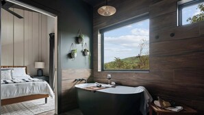Une salle de bain moderne avec une baignoire sur pieds, une grande fenêtre donnant sur un paysage verdoyant et un plancher en bois.
