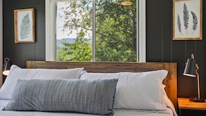A bed with white and gray pillows, a wooden headboard, and a window with a view of greenery. - Starstone Chalet - Hot Tub! Mountain Views! (Broadway)