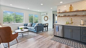 A modern living room with a sofa, coffee table, and a view of greenery outside. - Starstone Chalet - Hot Tub! Mountain Views! (Broadway)