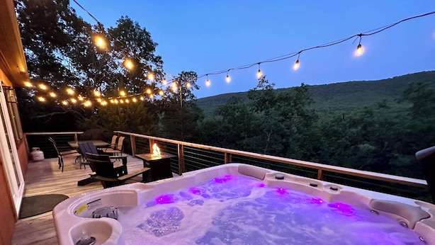 A hot tub with purple lighting on a wooden deck, surrounded by string lights and overlooking a forested area. - Starstone Chalet - Hot Tub! Mountain Views! (Broadway)