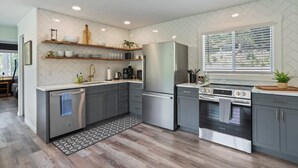 A modern kitchen with grey cabinets, stainless steel appliances, and a patterned rug. - Starstone Chalet - Hot Tub! Mountain Views! (Broadway)