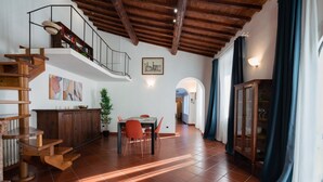 Une salle à manger spacieuse avec un haut plafond, un escalier en bois et une vue sur une autre pièce.
