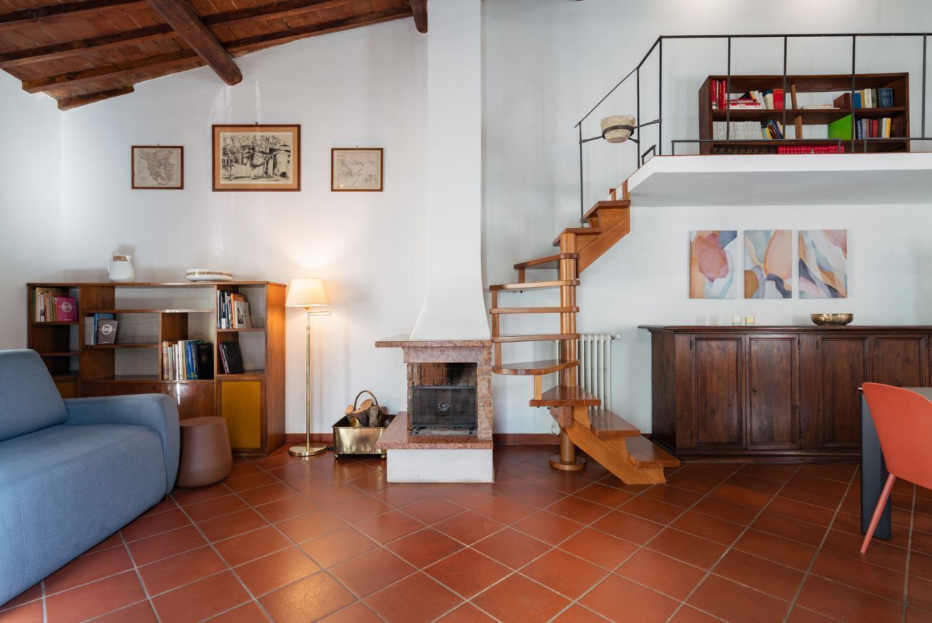 A living room with a sofa, a bookshelf, a fireplace, a staircase, and a dining area.