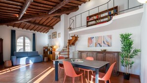 Un grand espace de vie comprenant une table à manger, des chaises, un canapé, un escalier et une bibliothèque.