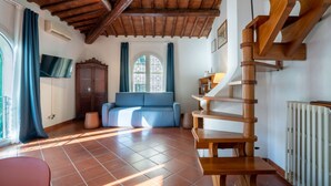 Une pièce avec un escalier en bois, un canapé bleu et un sol carrelé.