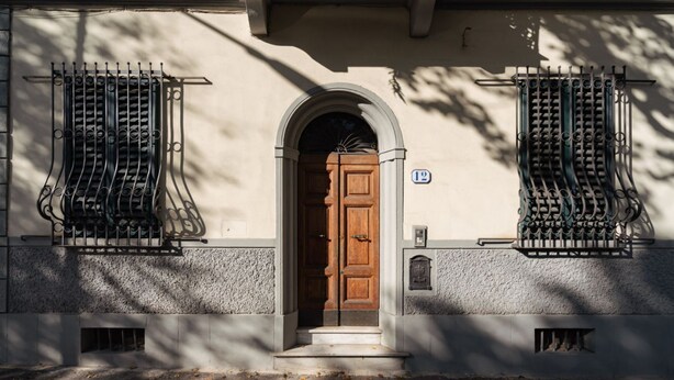 Un bâtiment avec une porte en bois, une plaque portant le numéro « 12 » et des grilles de fenêtre en fer forgé.