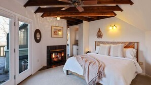 A bedroom with a fireplace, a bed with white linens, a ceiling fan, and a view through a glass door. - Slopeside Chalet: Ski & Bike in/out+Views+Hot Tub (Basye)