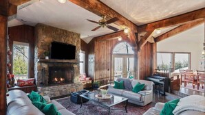 A spacious living room with a stone fireplace, wooden beams, a ceiling fan, and a piano. - Slopeside Chalet: Ski & Bike in/out+Views+Hot Tub (Basye)