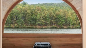 Una sauna con un banco de madera y vistas a una ladera boscosa a través de una abertura en arco.