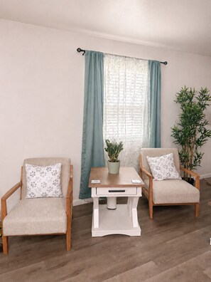 A room with two armchairs, a small table, a potted plant, and a window with curtains.