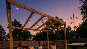 En træterrasse med udendørs møbler, lyskæder og en træpergola.