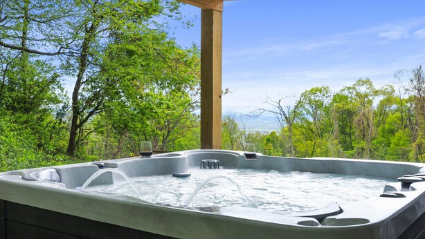 Un bain à remous doté d’une structure en bois, offrant une vue sur une végétation luxuriante et des montagnes en arrière-plan.