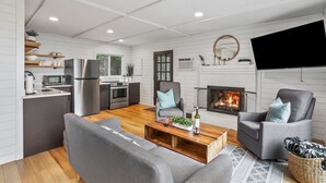 A modern living room with a fireplace, grey sofas, a coffee table, and a kitchen area with a fridge, microwave, and stove. - Mountain View Cabin~HotTub~Fireplace~King Bed (New Market)