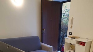 Ein Zimmer mit einer Couch, einem Fernseher auf einem Schrank, einem weißen Schrank mit Schubladen und einer Tür, die nach draußen führt.