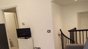 Ein Wohnzimmer mit einem blauen Sofa, einer weißen Kommode mit Fernseher und einer Treppe.