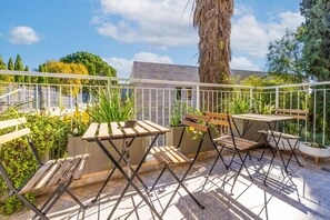 A balcony with a wooden table and chairs, potted plants, and a view of buildings and trees. - Exclusive&Lovely Apartment in Prestigious Talbiya (Jerusalem)